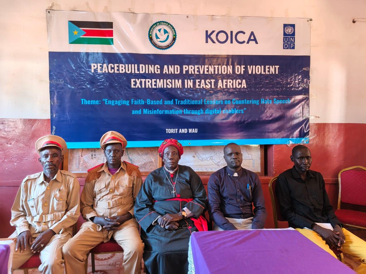 Six men sit before a banner about peacebuilding in East Africa; KOICA and UN logos.