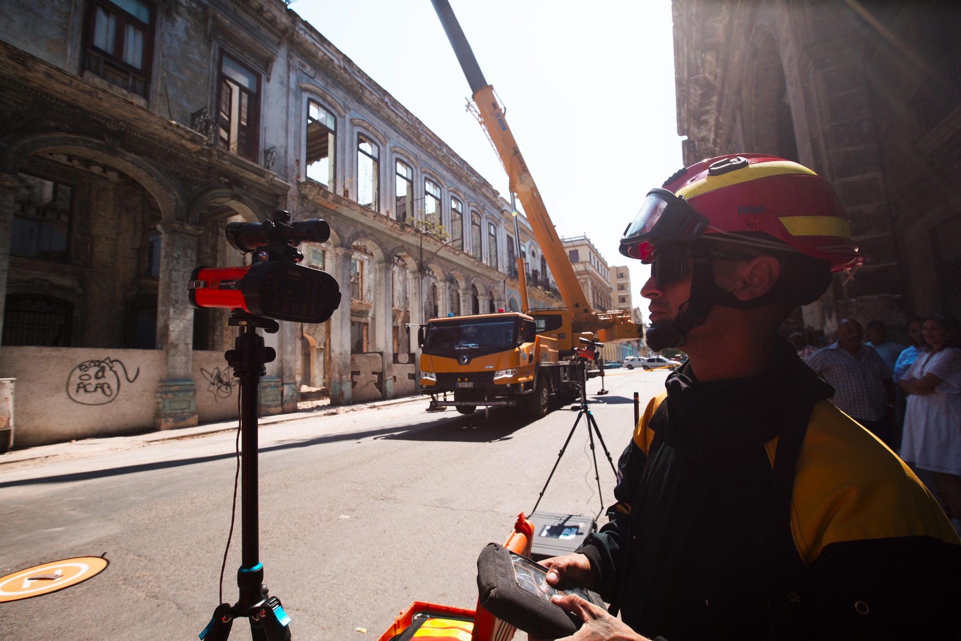 Helmeted worker in reflective gear on a city street with a crane and a bus in the background.