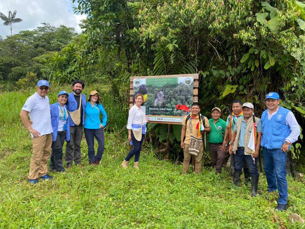 Group photo of people standing on grass with a banner behind them, trees in the background.