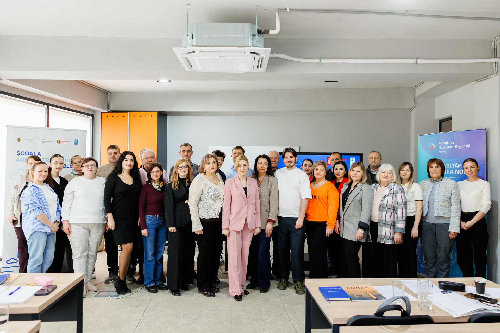 Diverse group posing for a photo in a classroom-style training room with projectors.