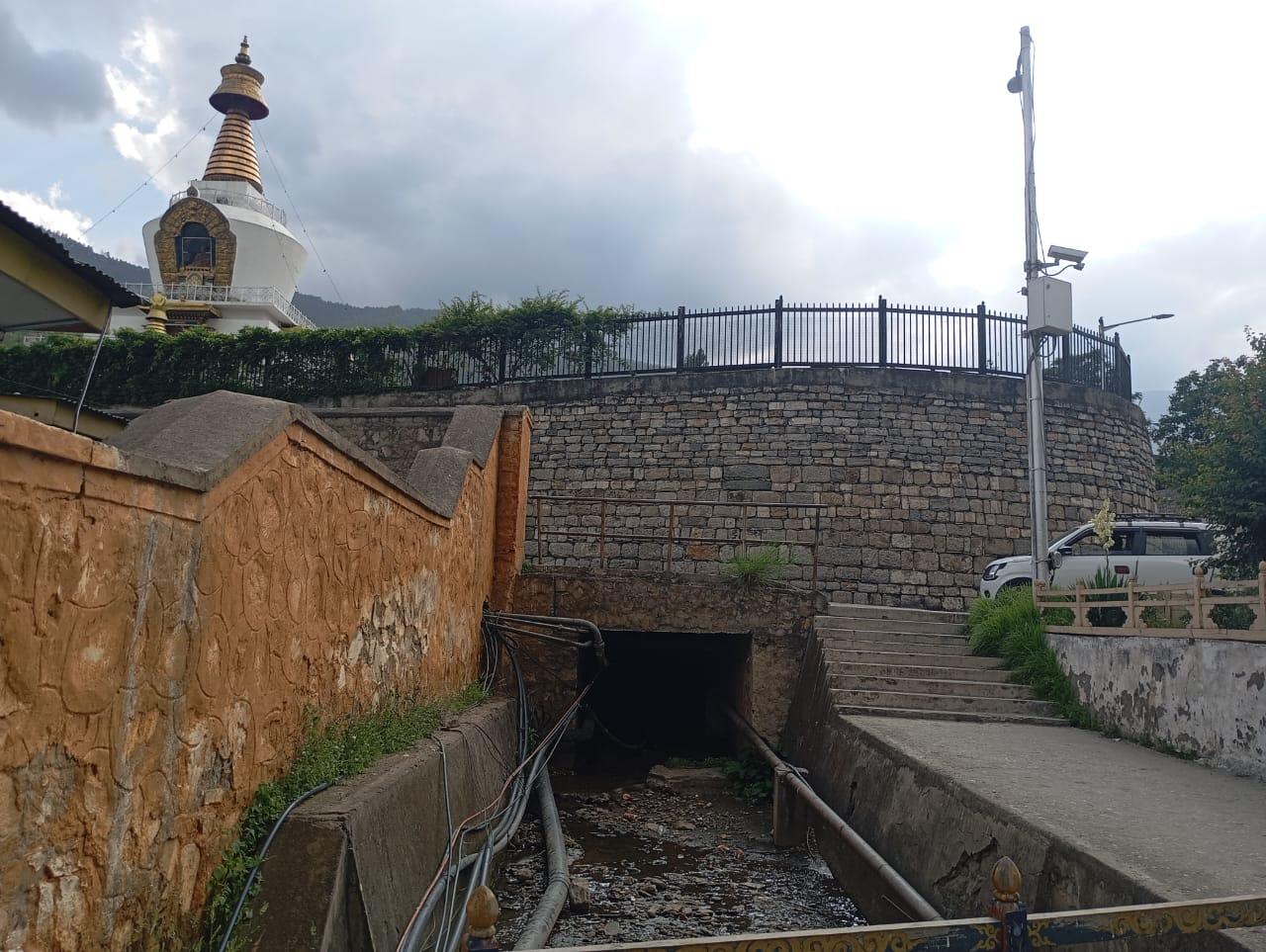 Stone terrace, rectangular drainage channel, and railing; a small domed building on the left.