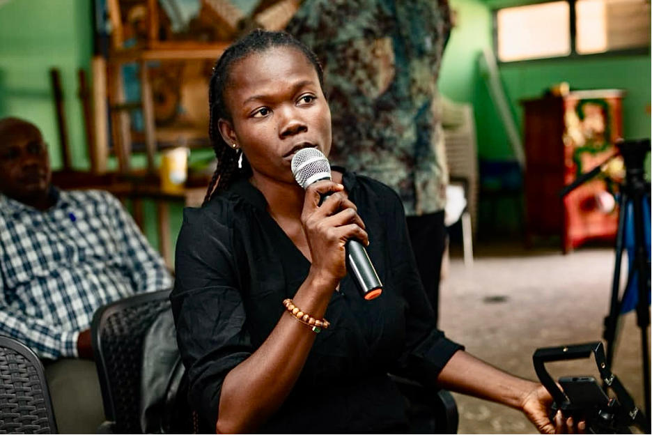 Woman with microphone at a discussion; others seated nearby.