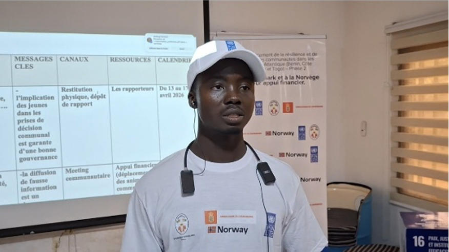 Man in white tshirt, standing by a presentation screen and banner.