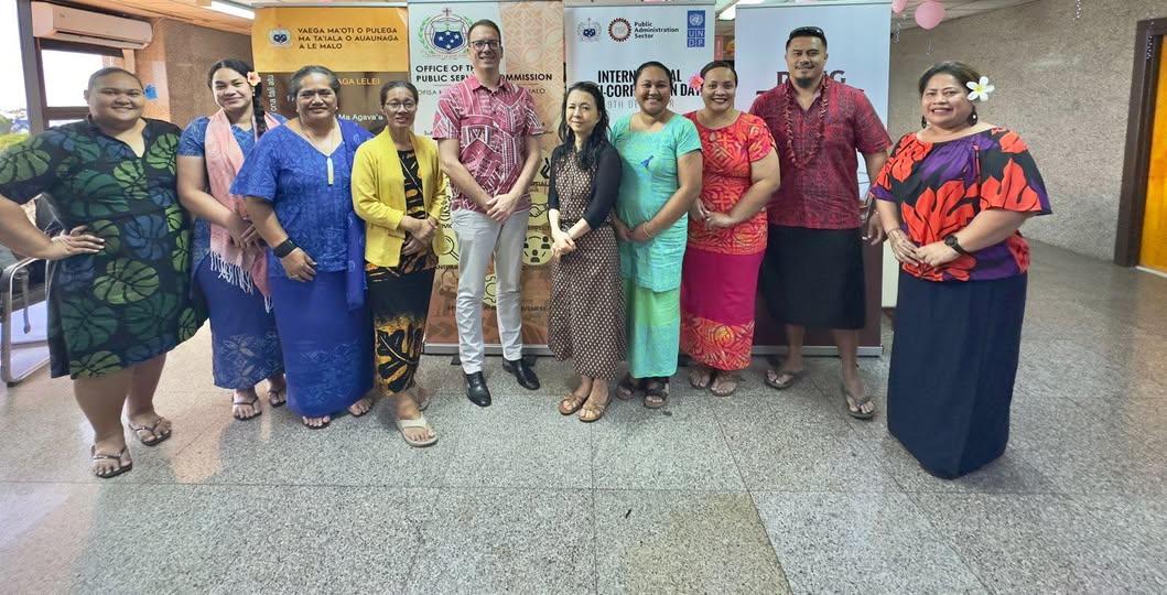 Group photograph of men and women in colorful traditional Indian attire posing in a hallway.