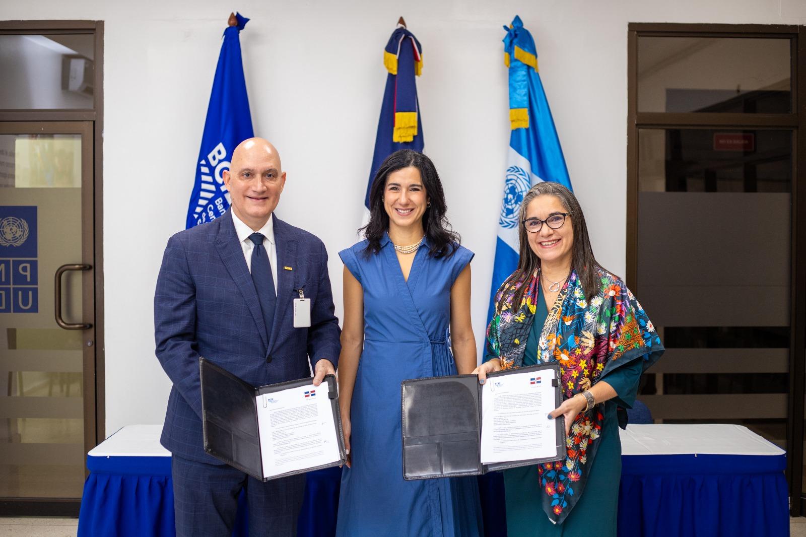 Photo: three smiling adults pose with certificates in front of blue flags.