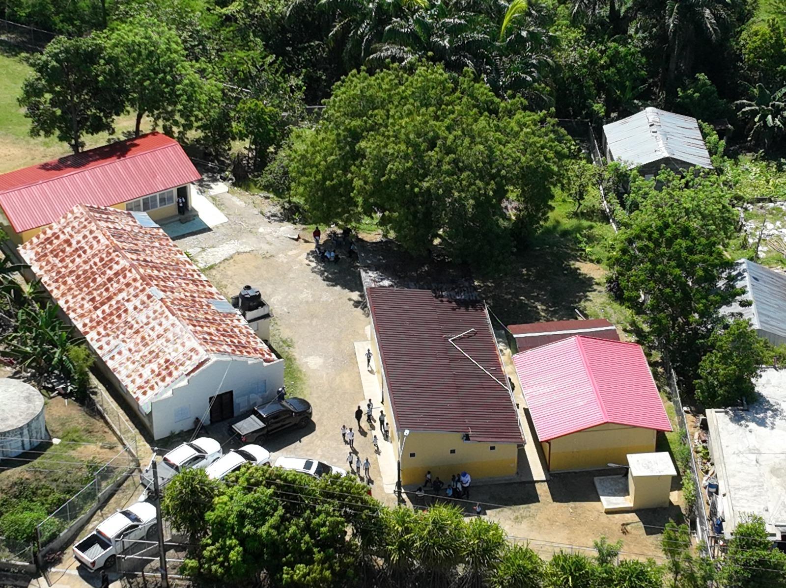 Aerial view of a rural village with red, yellow, and white roofs among trees; people on a path.