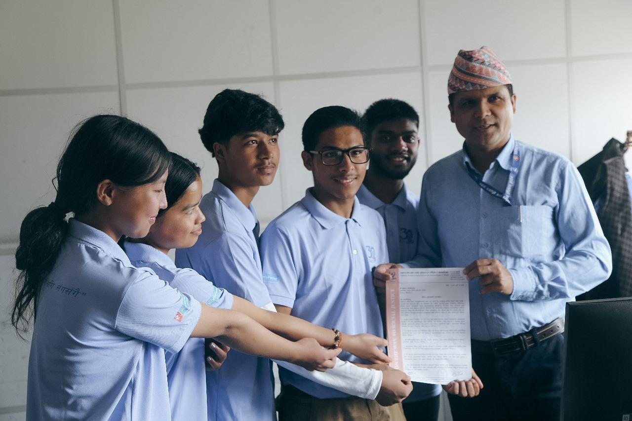 Group of students in light blue uniforms presenting a document to a man wearing a turban.