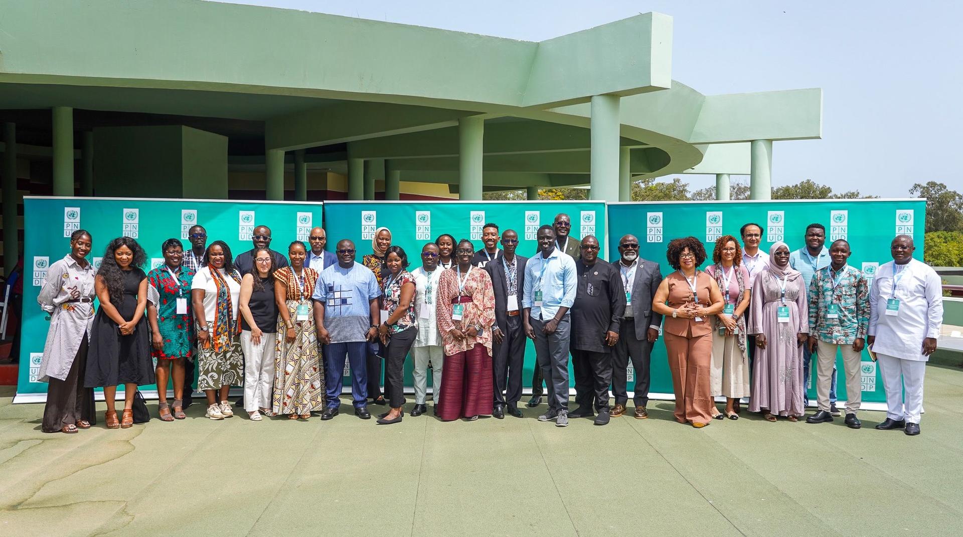 Group of people in traditional attire posing outdoors in front of a green building.