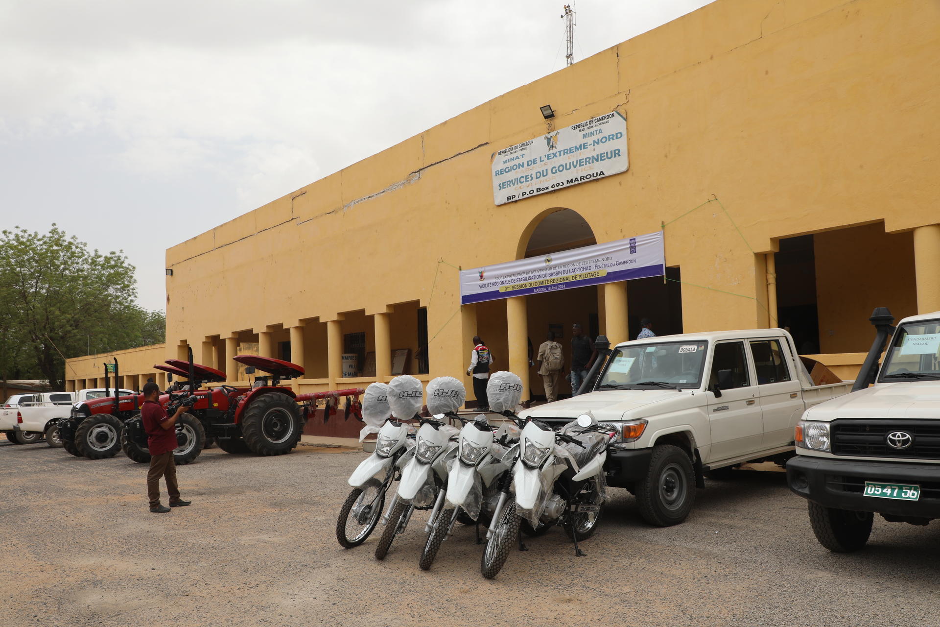 Photo of a yellow building with a sign, front area filled with motorcycles and parked cars.