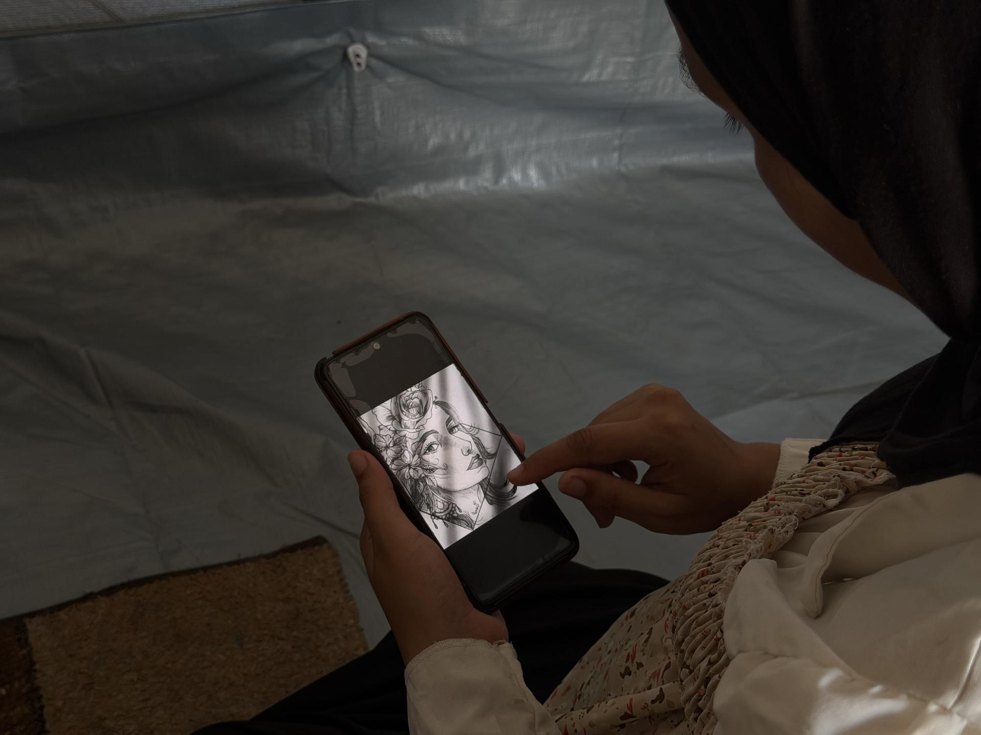 Person in a headscarf using a smartphone inside a dim tent.