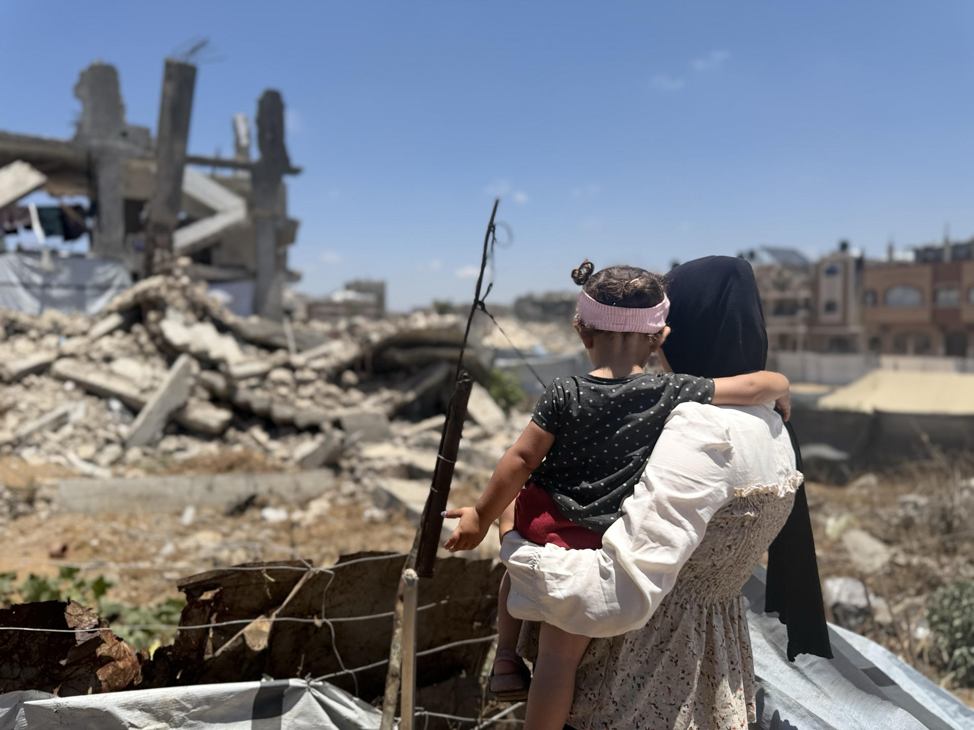 Photograph: woman carrying a child amid rubble and wooden beams at a construction site.