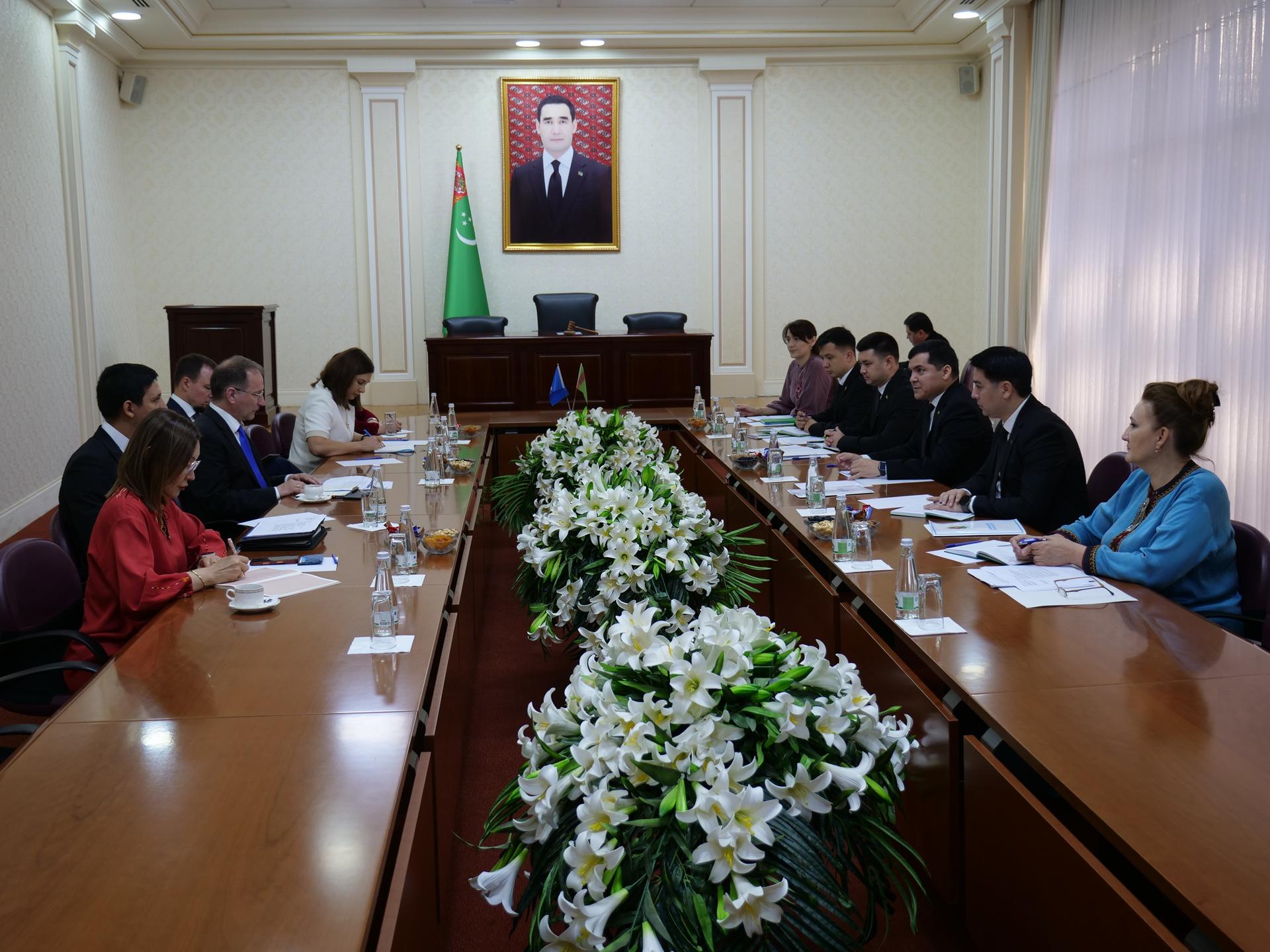 Formal meeting in a conference room with a long table, white flower centerpiece, and attendees.