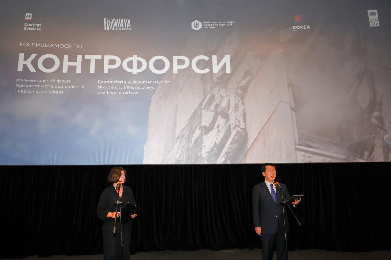 Photo: two men in suits on a stage, a large screen with Cyrillic text behind them.