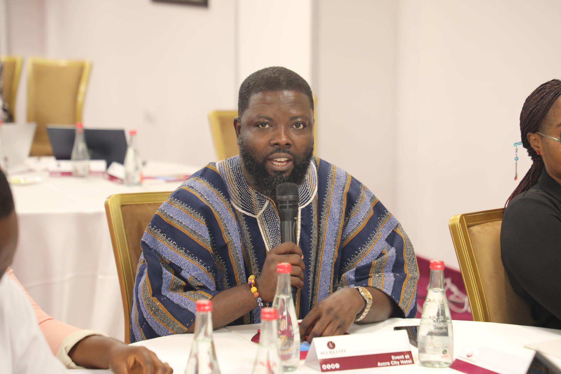 Man in striped traditional attire speaks into a microphone at a conference table.