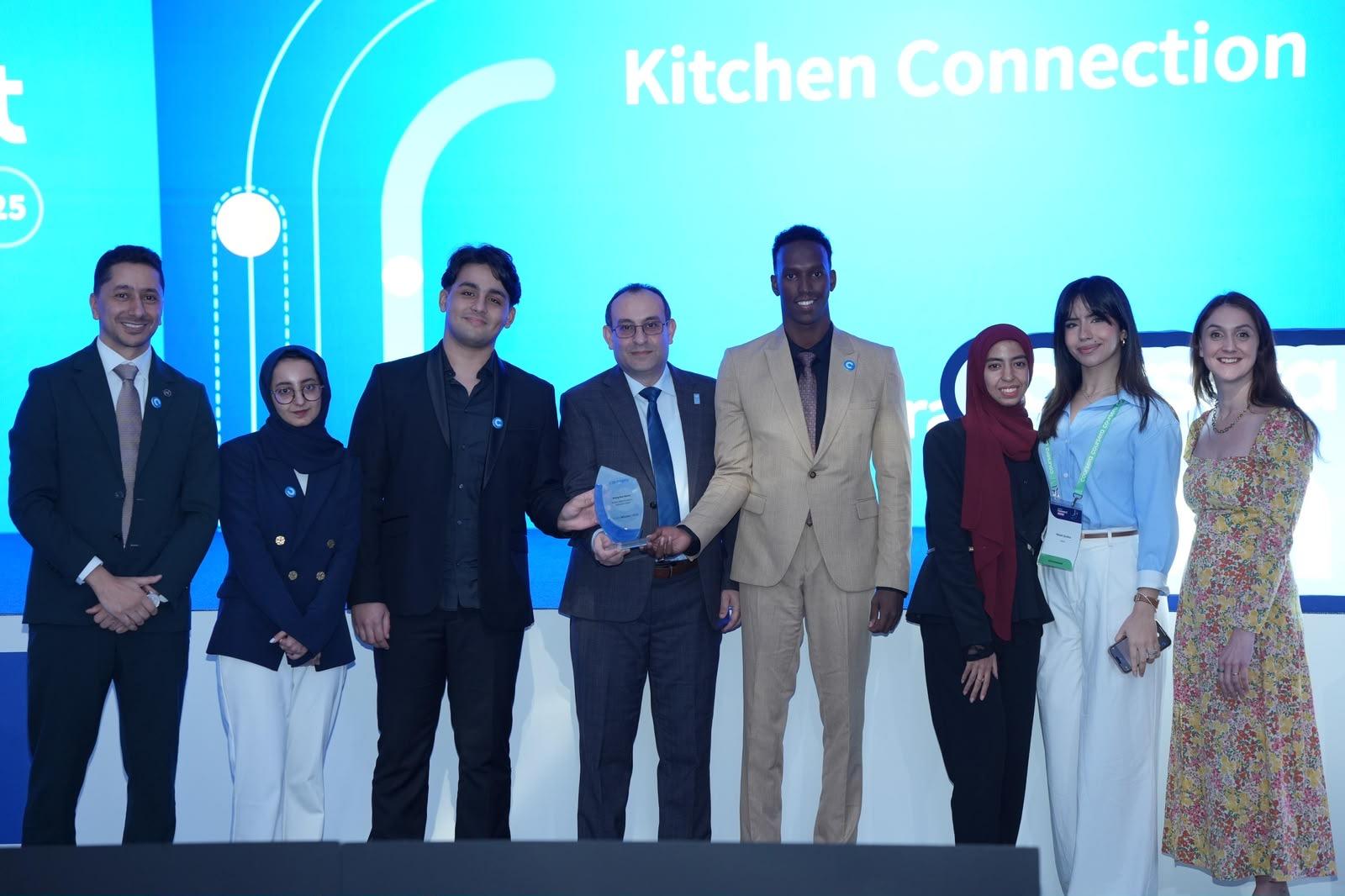 Group of people on a stage posing in front of a blue Kitchen Connection backdrop.