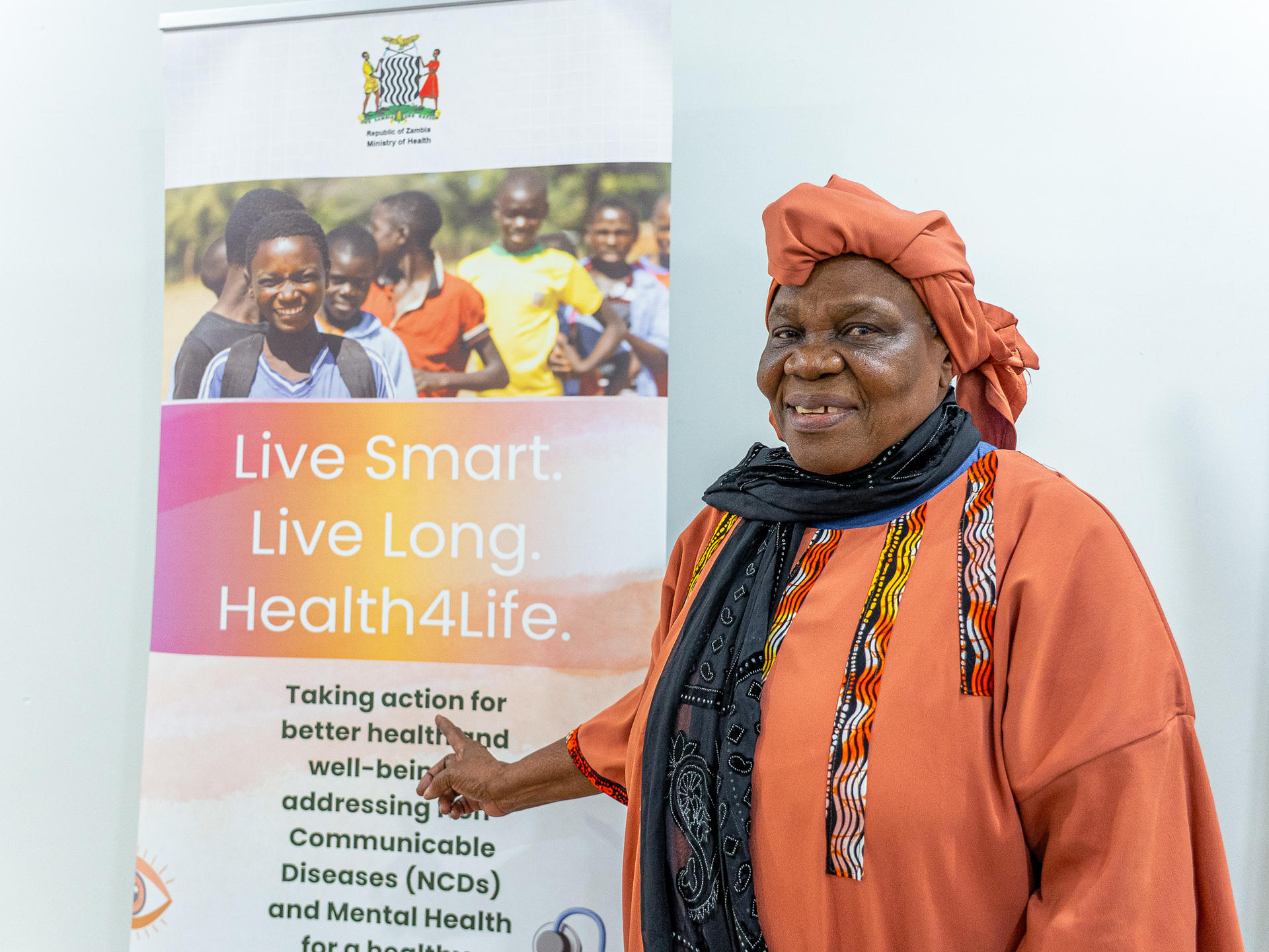 Portrait of a woman in orange traditional dress beside a health awareness banner.