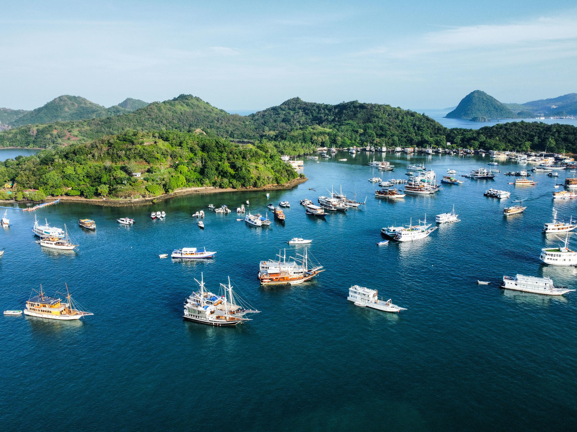 Aerial view of a blue harbor with many sailboats anchored among green hills.