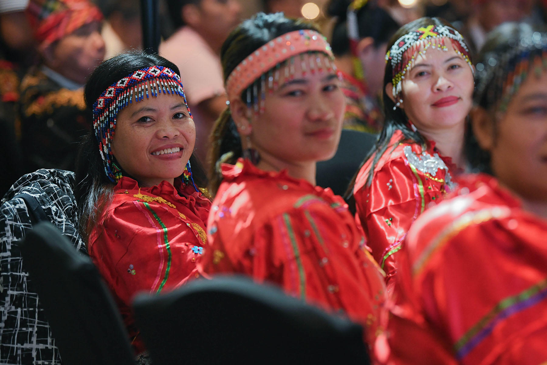 Group of people in red traditional outfits with beaded headbands, smiling at a cultural event.