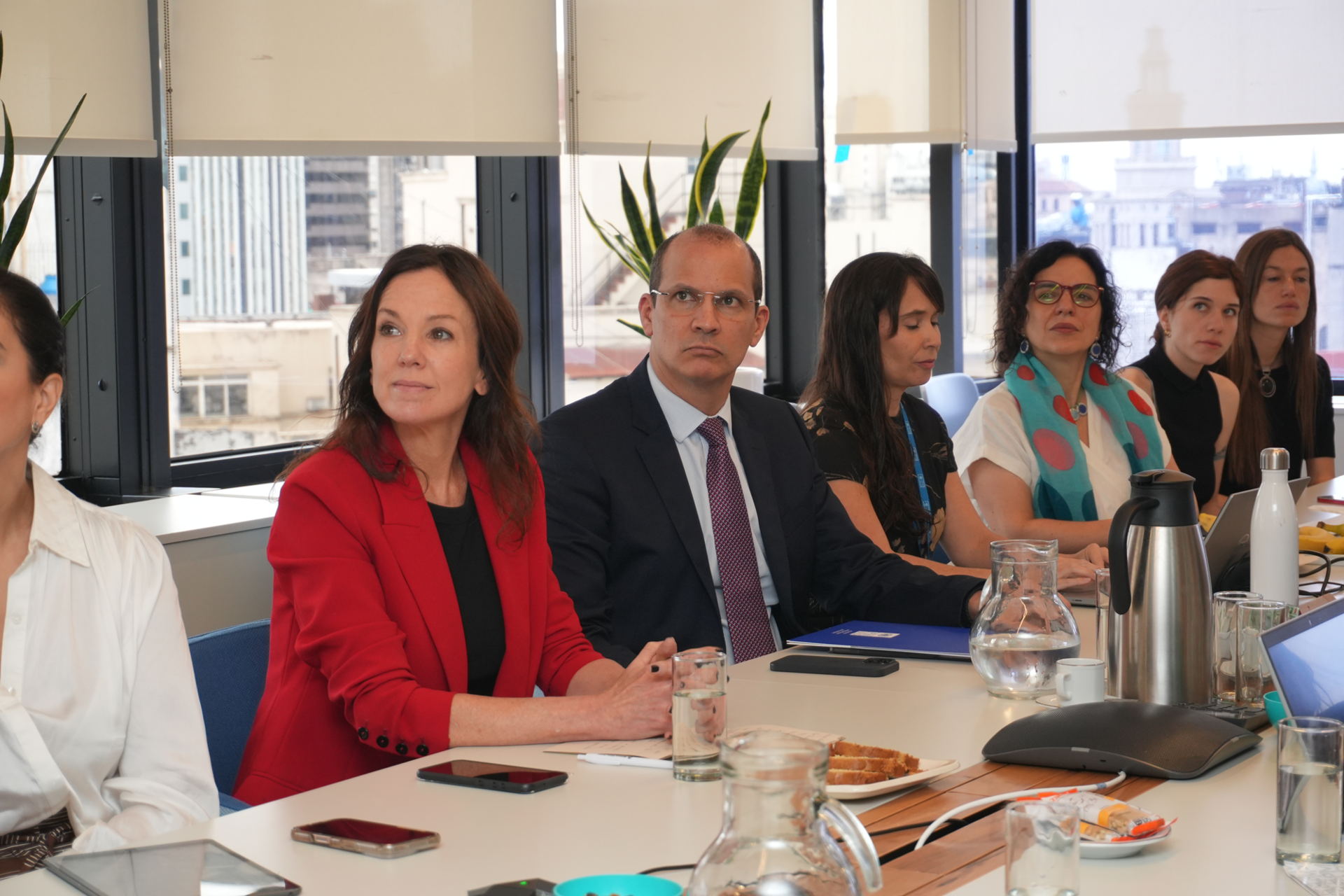 Photograph of professionals at a conference table; a woman in a red blazer sits near the center.
