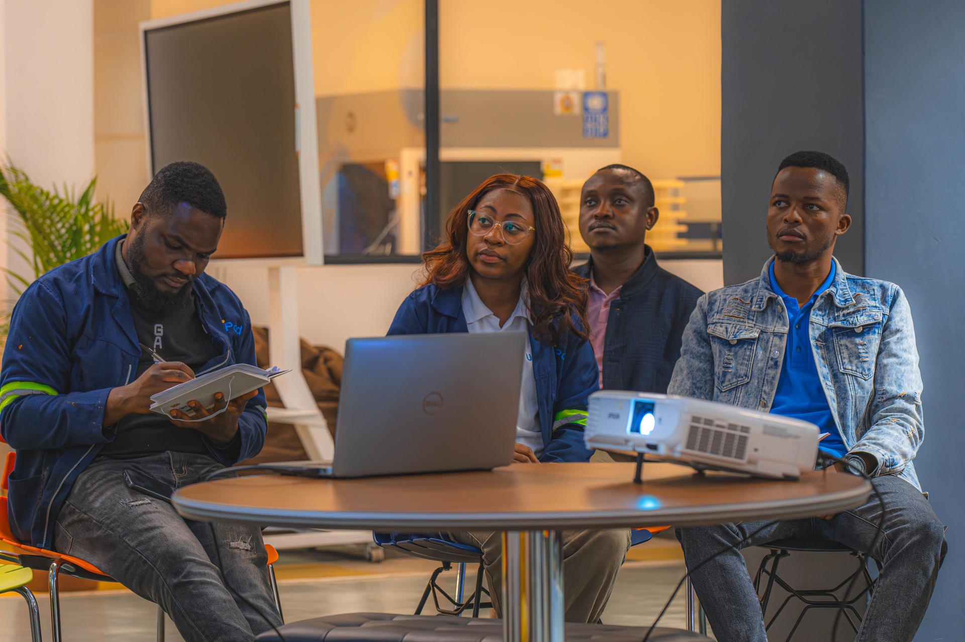 Four colleagues sit around a table with a laptop and projector in a bright office.