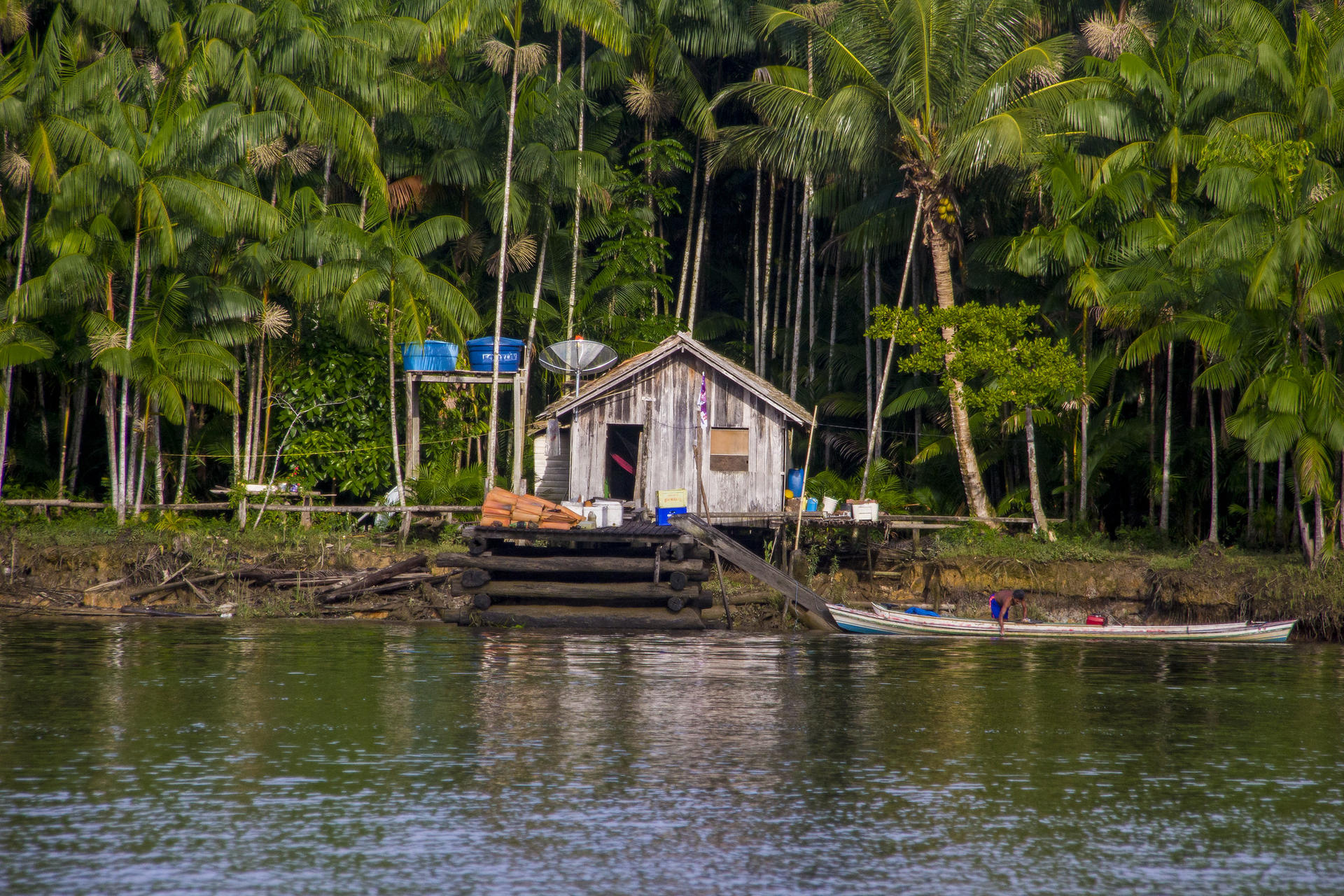 Small wooden cabin on a dock over calm water, surrounded by tropical trees.