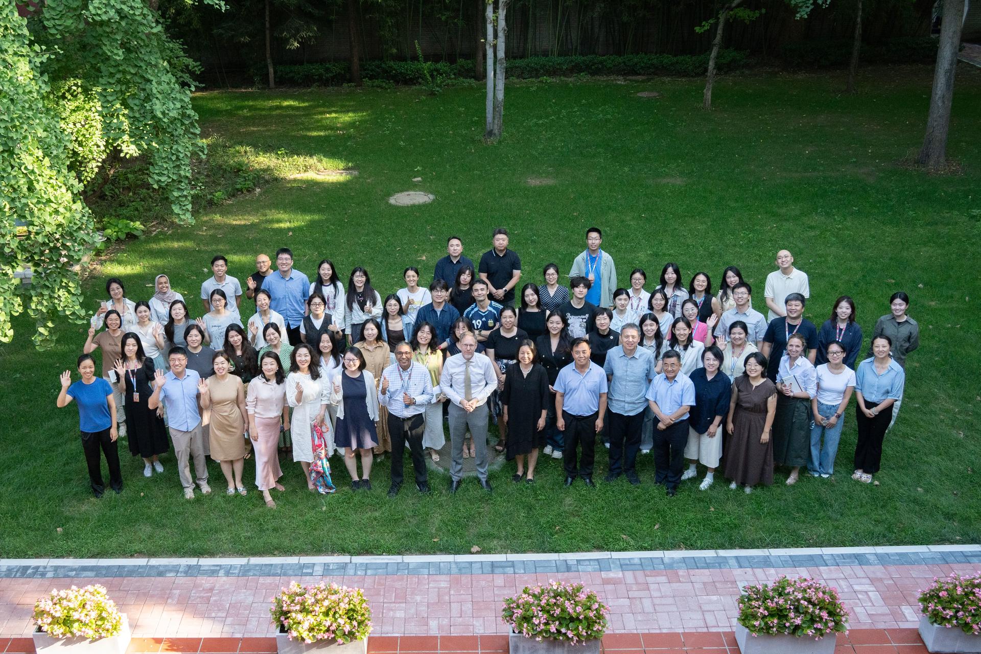Large group of people posing outdoors on a grassy lawn with trees in the background.