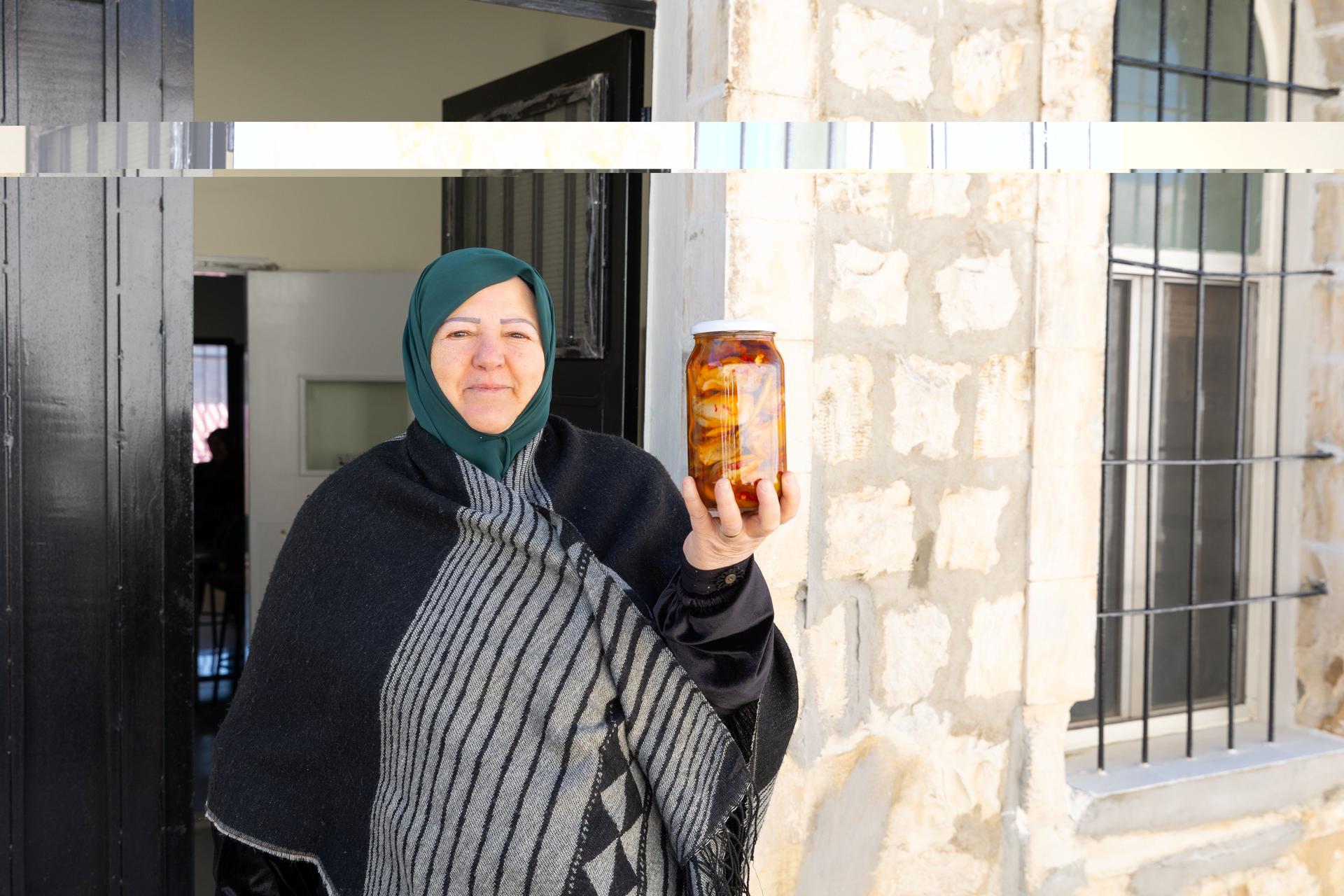 Woman in teal headscarf and striped shawl holding an amber bottle outdoors.