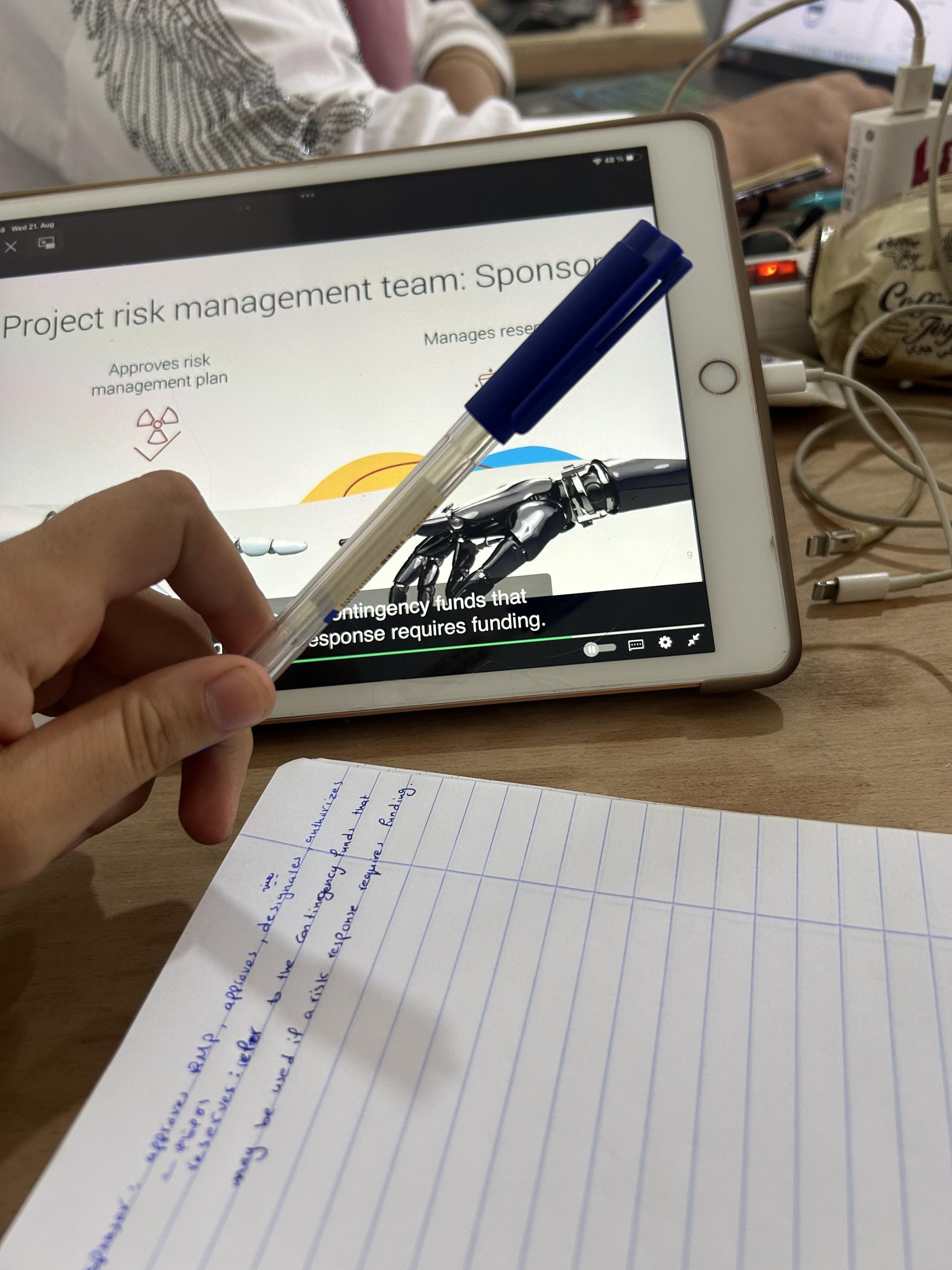 Hand holding blue stylus pointing at tablet screen displaying project risk management slide.