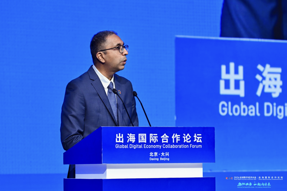 Photograph of a man in a suit giving a speech at a blue conference podium with Chinese text.