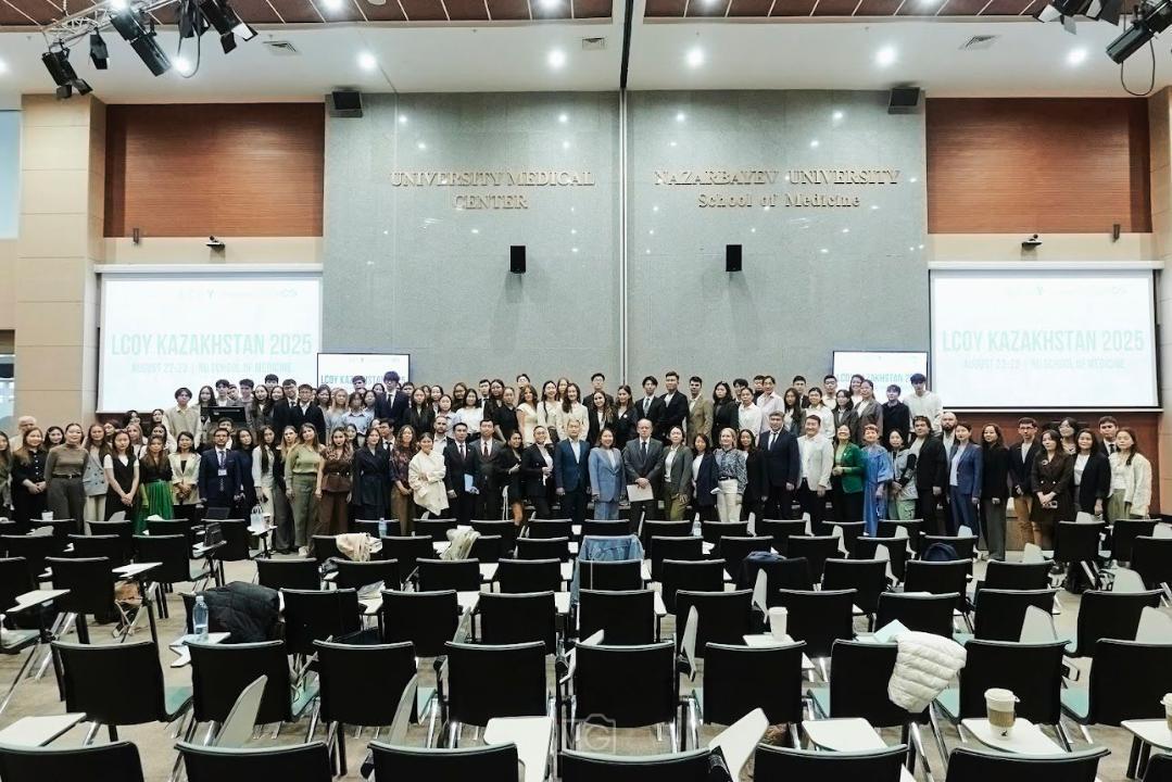 Group of attendees posing for a photo in a conference hall with empty chairs in the foreground.