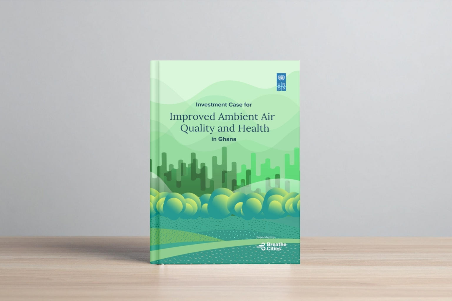 Green book on a wooden table, with a city skyline and blue waves on the cover.