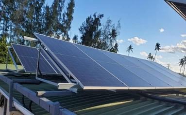 Tilted solar panels on a rooftop, with blue sky and trees in the background.