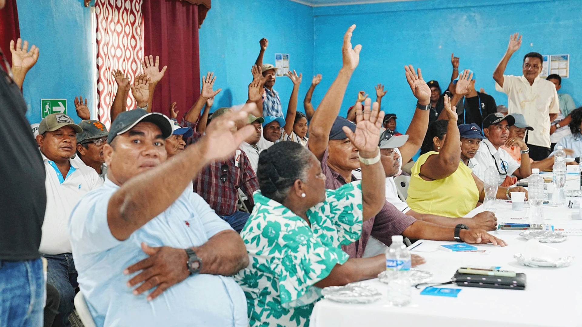 Photograph of a group at a long conference table, raising hands in celebration.