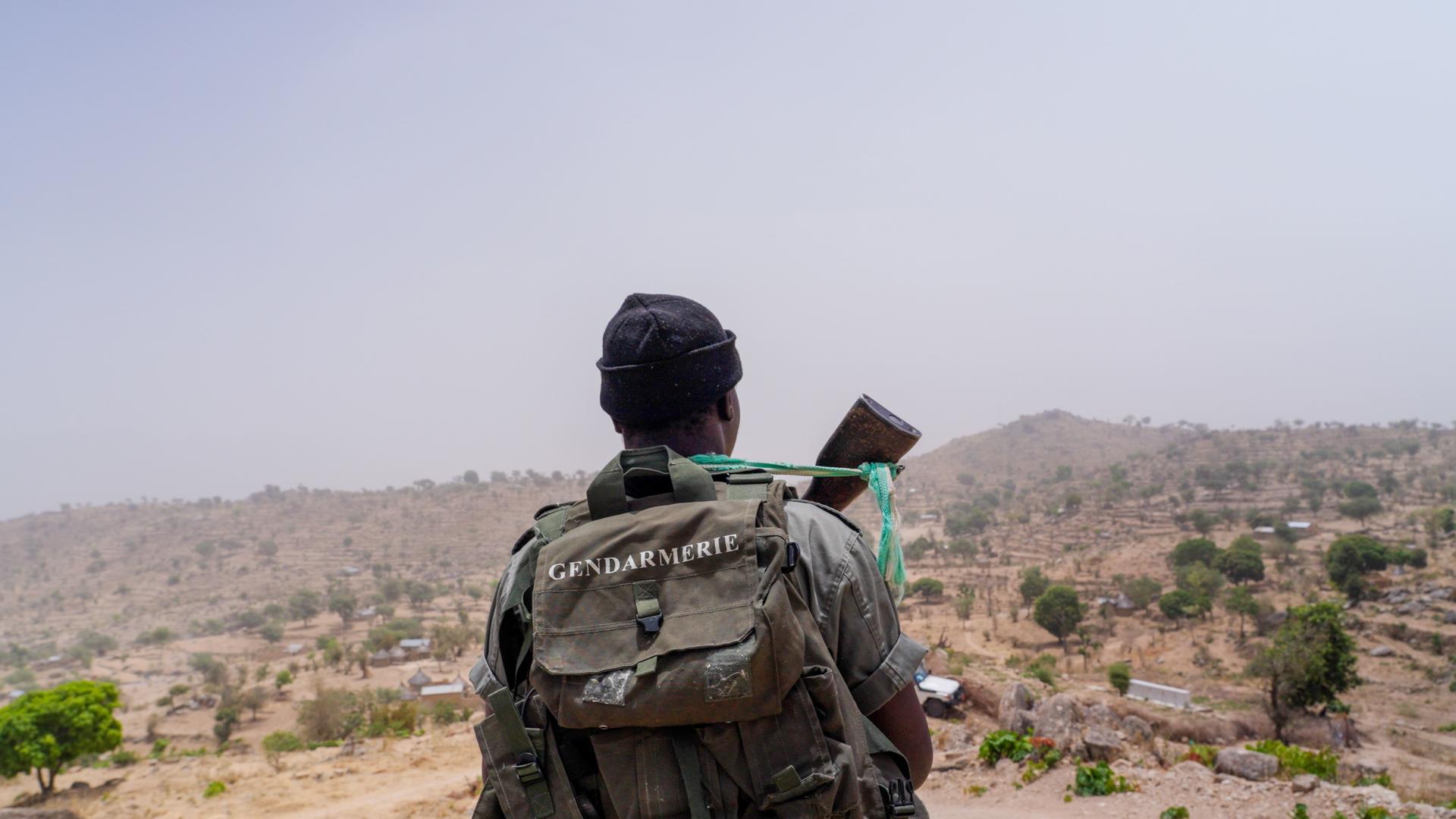 Hiker with a backpack stands in a desert, looking at a map amid rocky hills.