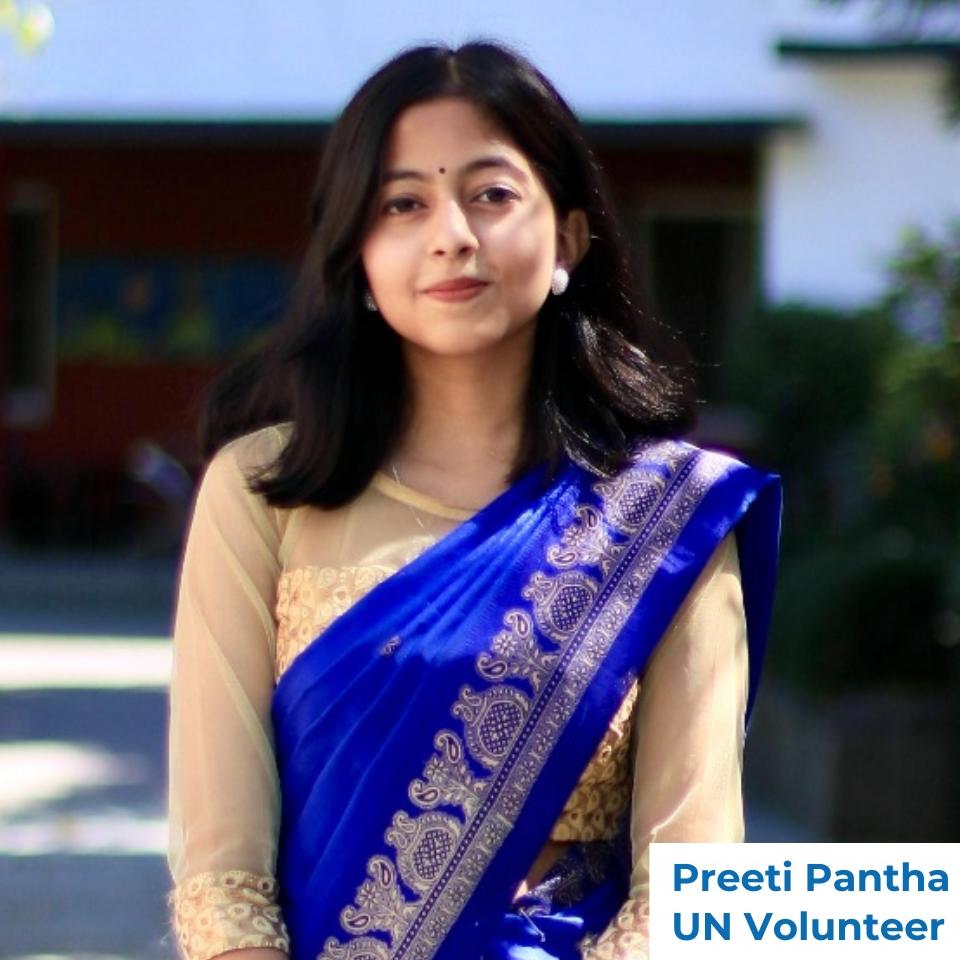 Portrait of a woman in a blue saree with gold border, standing outdoors.