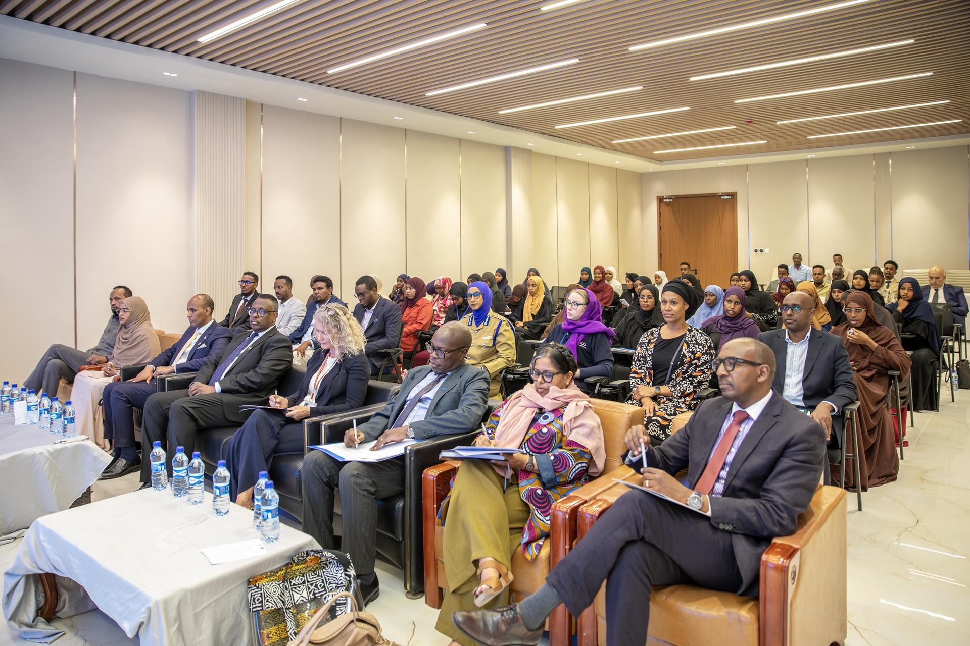Audience seated in a well-lit conference room for a seminar; front row in suits.
