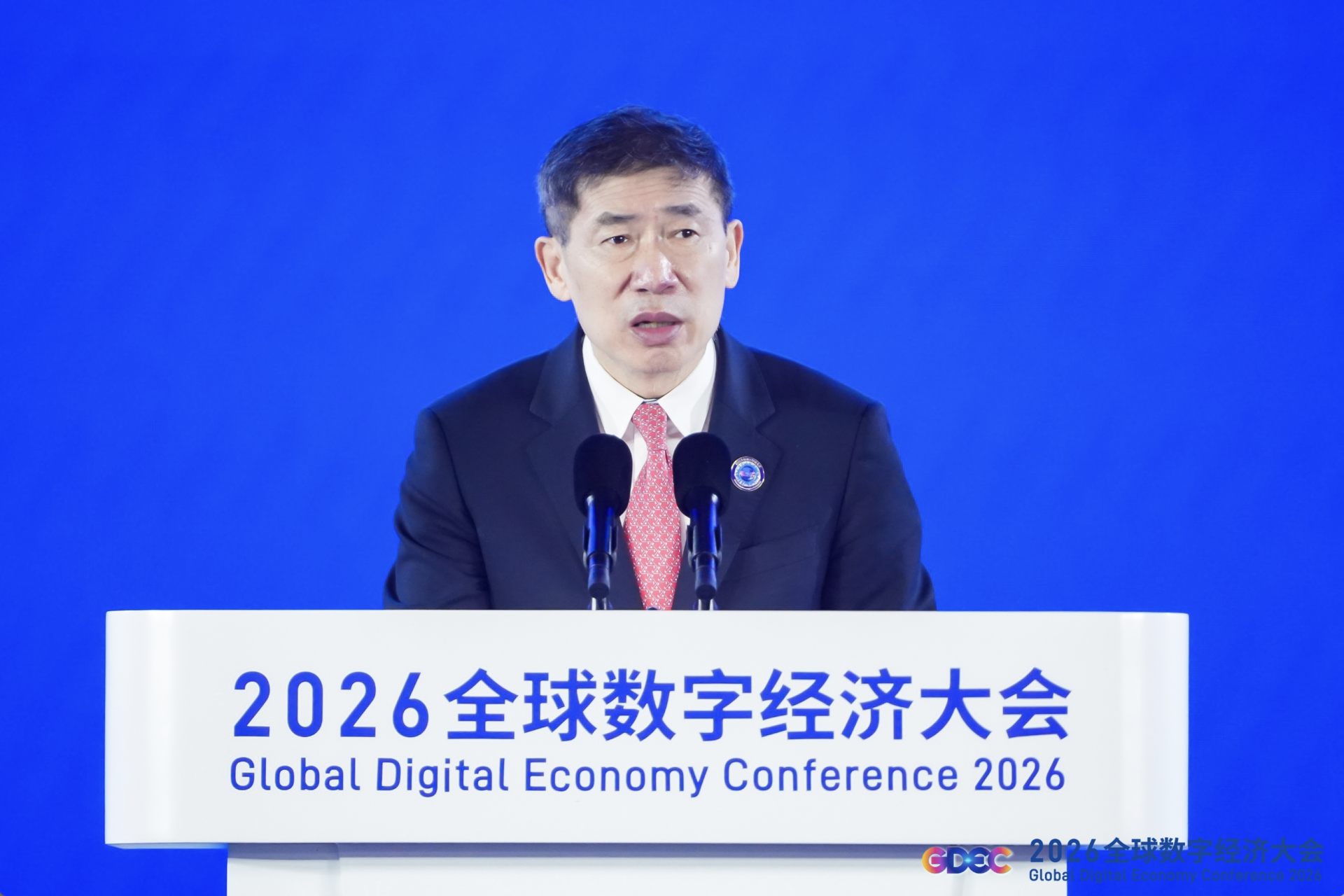 Photo of a man speaking at a podium with a blue backdrop; sign reads 2026 Global Digital Economy Conference.