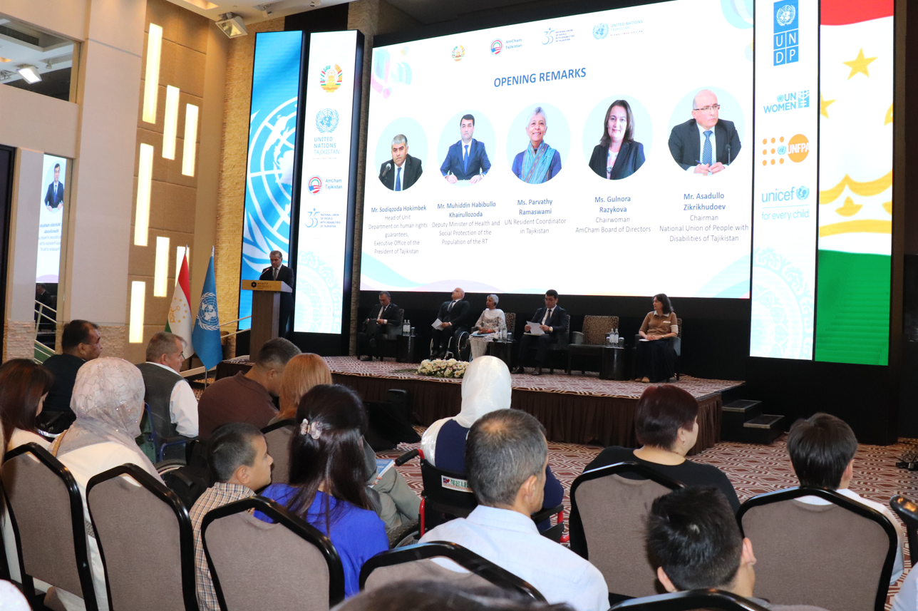 Photo of a conference panel on stage with large projection screens and an audience.