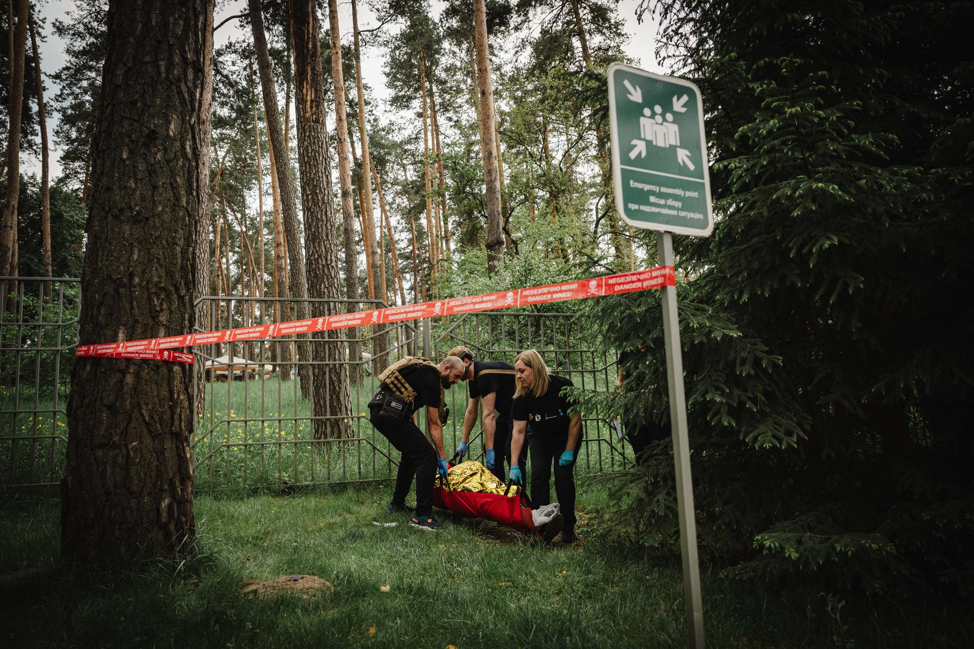 Emergency responders carry a patient on a yellow stretcher through a forest, red tape in background.