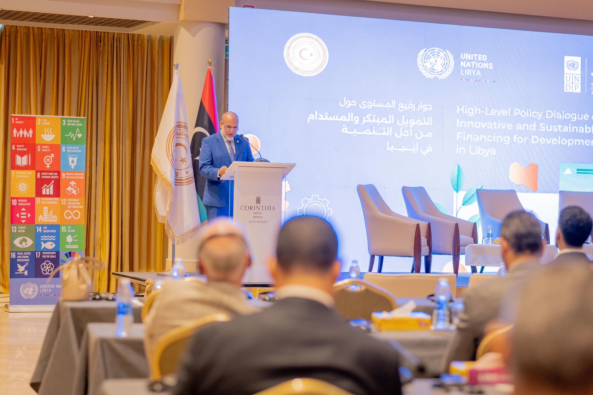 Photograph of a speaker at a podium on stage at conference; audience seated; UN logos on backdrop.