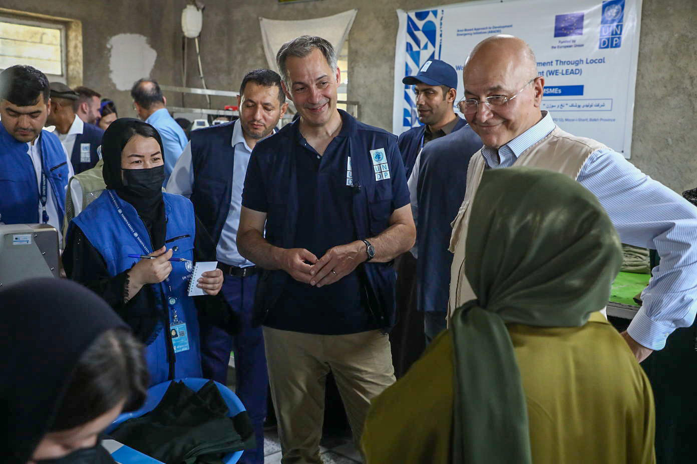 Diverse group at a community event; man in blue shirt speaks to a woman in green headscarf.