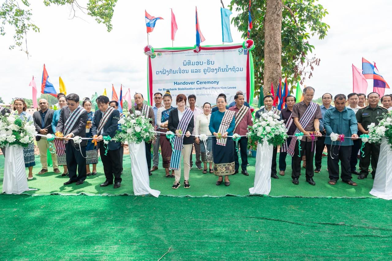 Group of formally dressed people posing outdoors under a banner with flags and flower arches.