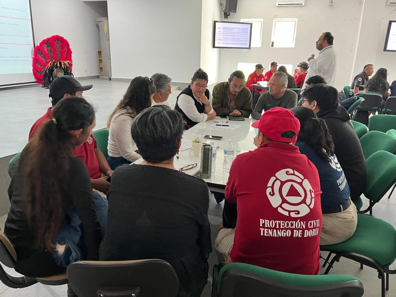 Group around a table in a classroom, discussing; foreground wears red hoodie with white logo.