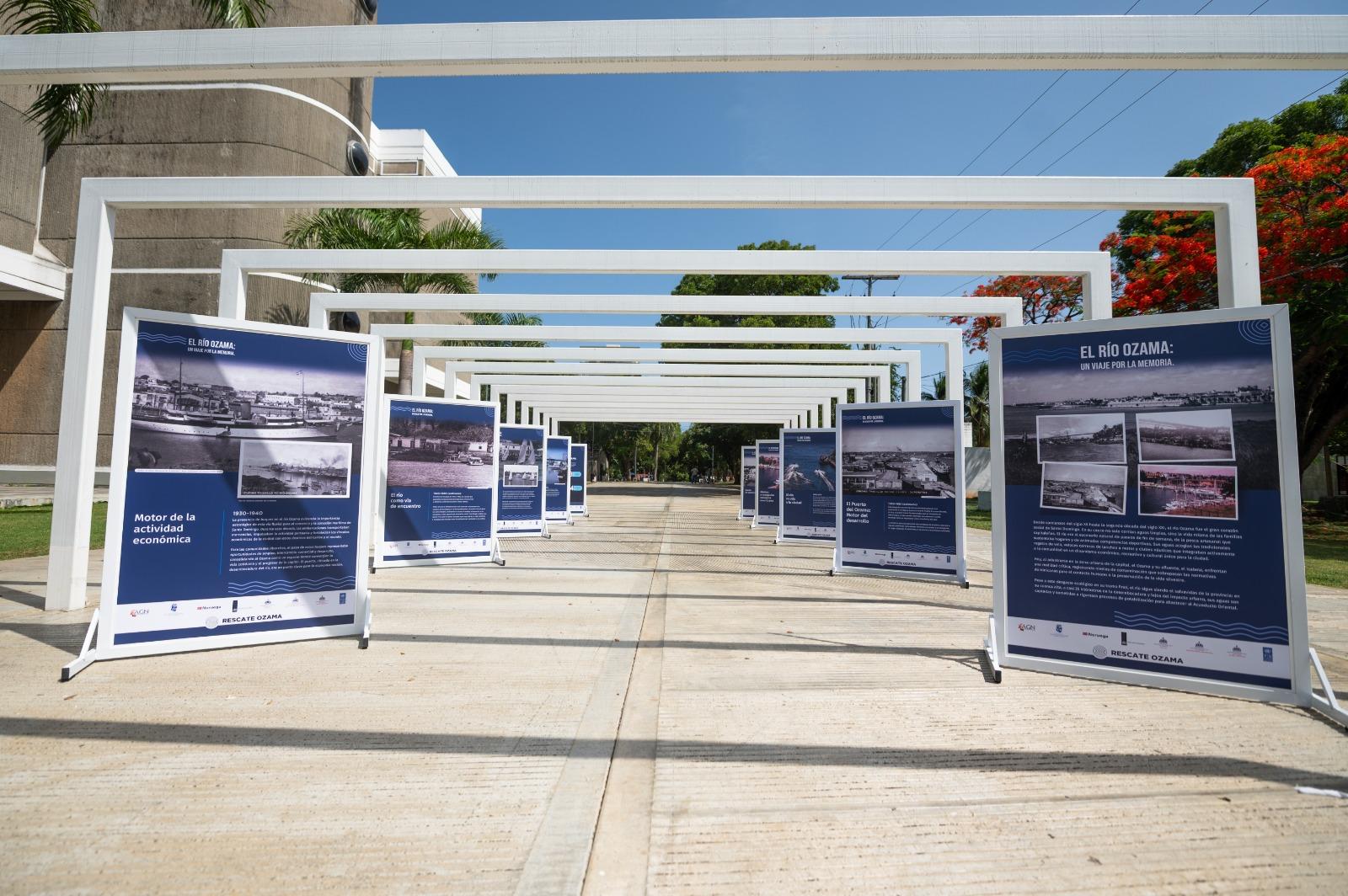Sunlit outdoor walkway lined with white metal frames and blue display panels.