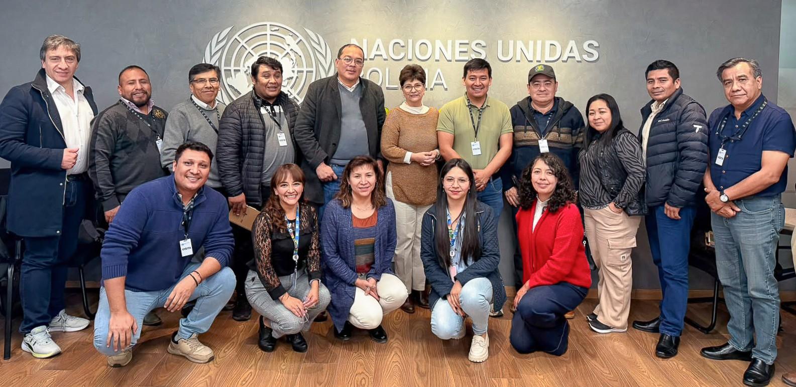 Group of diverse people posing for a photo in a conference room with a United Nations banner.