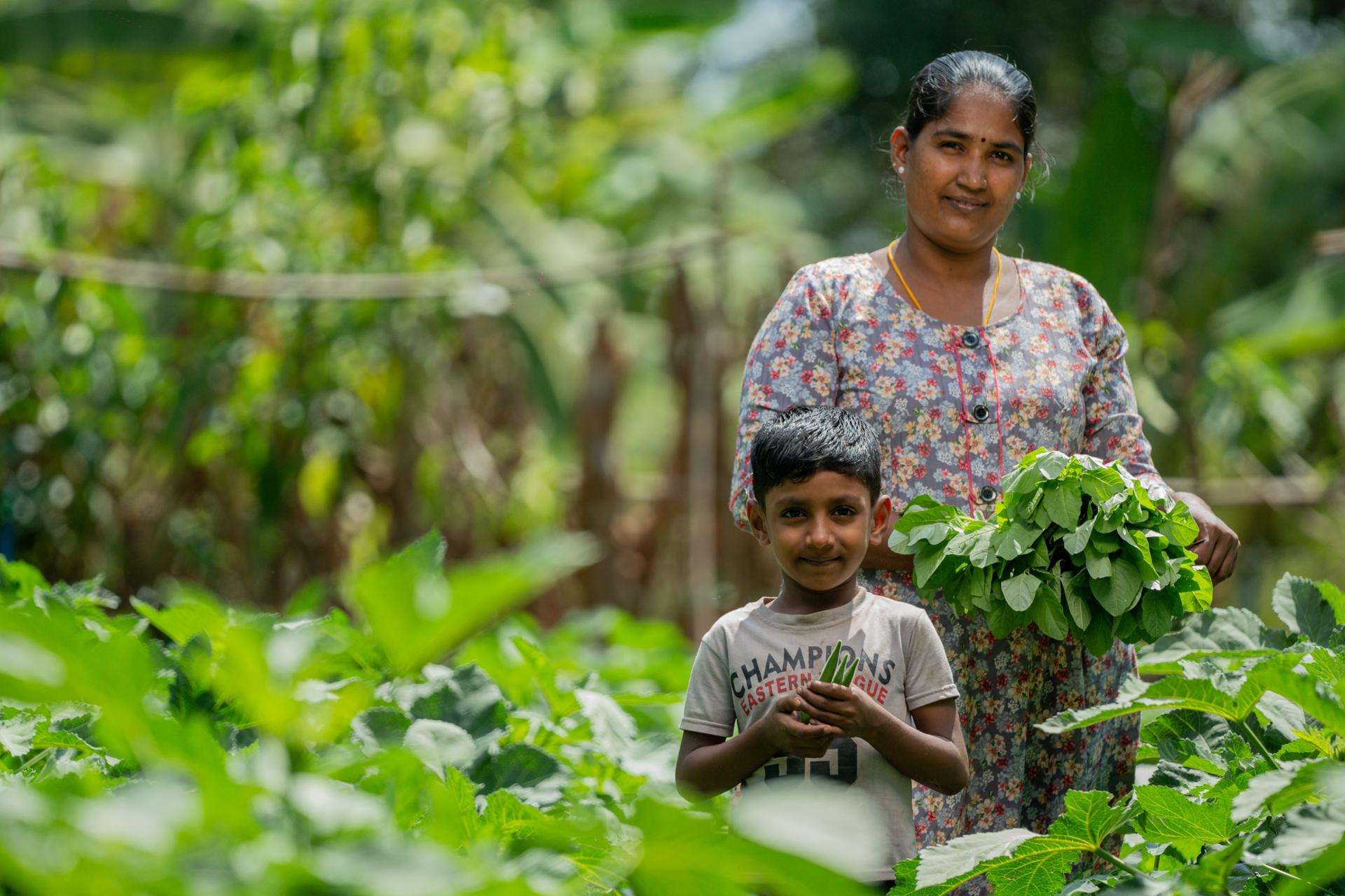 Photograph: mother and child in a lush garden, smiling among leafy greens.