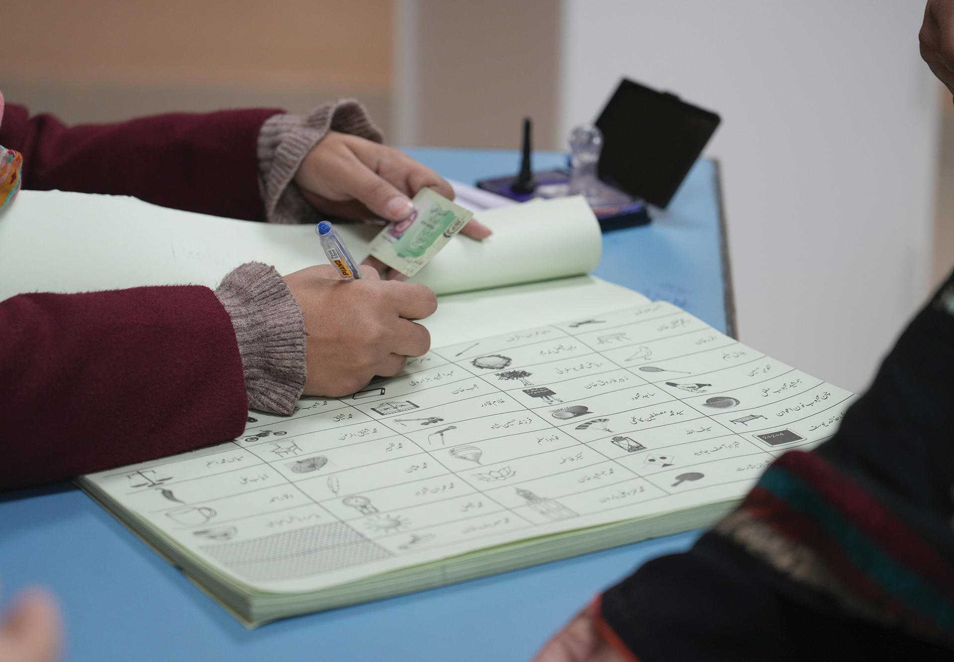 Close-up of hands signing a document on a blue desk, with a laptop in the background.