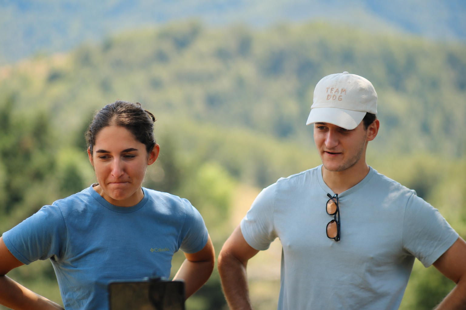 Photograph of two hikers, a woman and a man, looking at a device outdoors with hills behind.