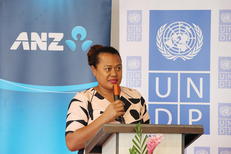 Photograph of a woman speaking at a podium with UNDP and ANZ banners.