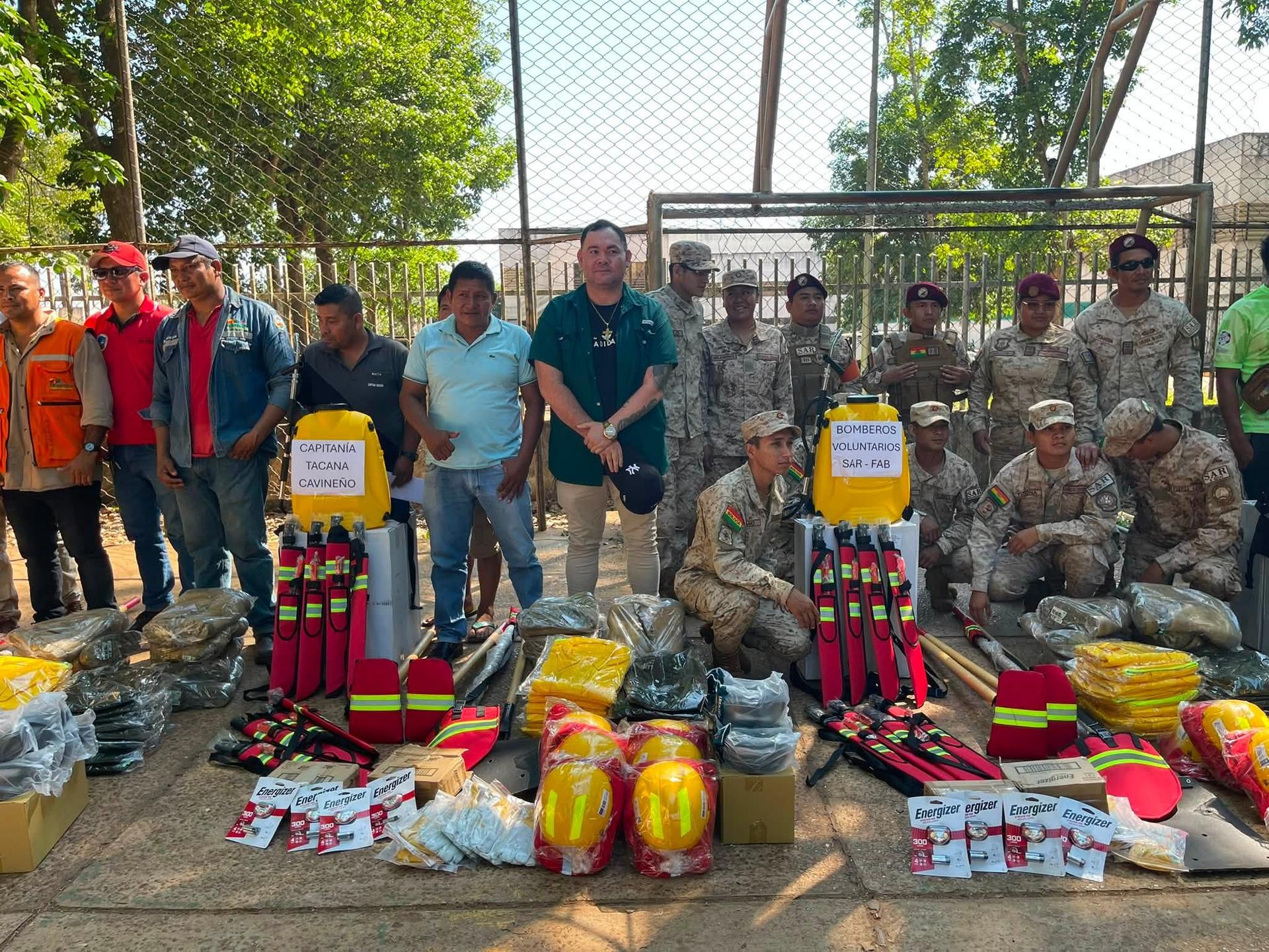 Group of soldiers and civilians pose with aid supplies on an outdoor court.
